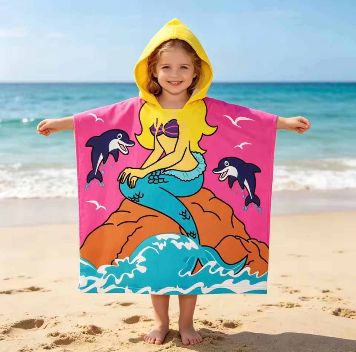 Girl wearing the Mermaid & Dolphin poncho towel with a mermaid and dolphins, yellow hood, at the beach, in microfiber